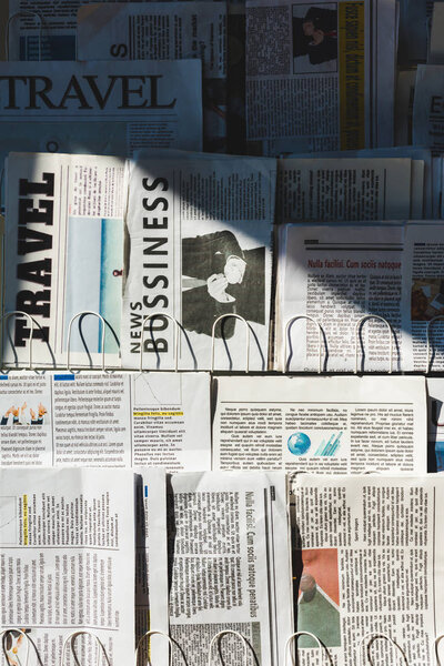 different print business and travel newspapers on stand in sunlight