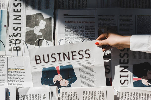 partial view of woman taking daily print business newspaper from stand