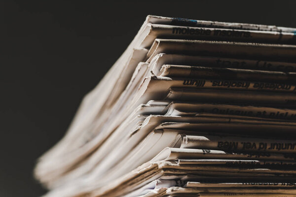 different print newspapers in pile isolated on black