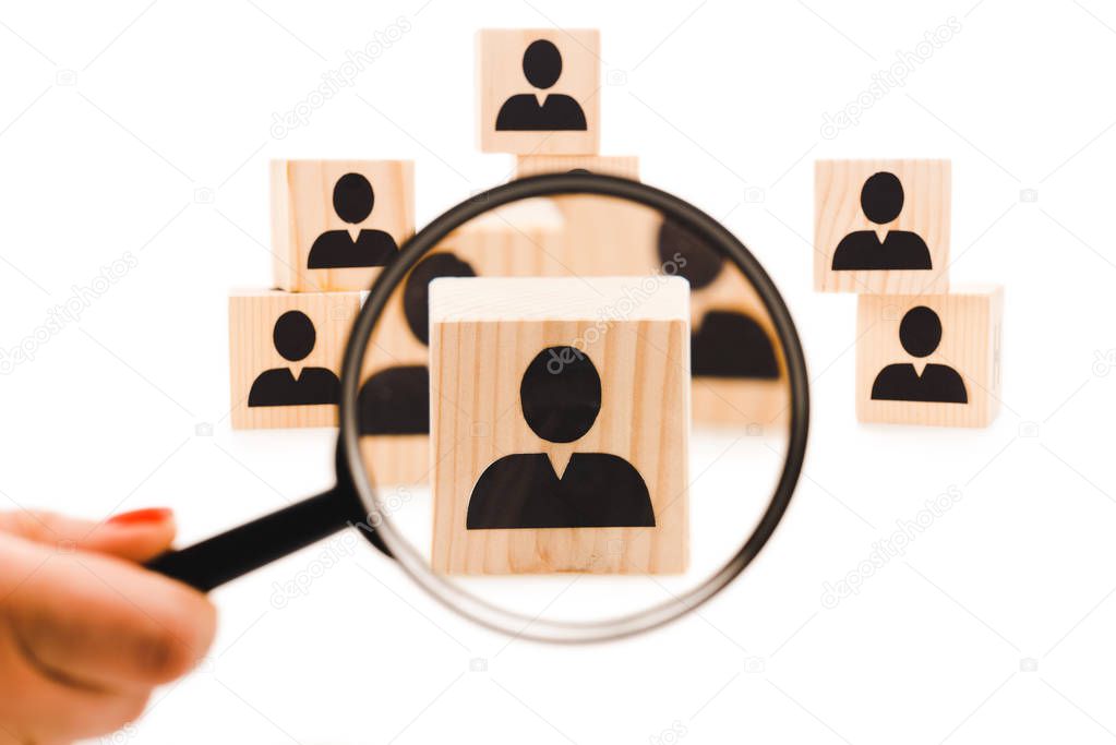 cropped view of woman holding loupe near wooden block with black human icon isolated on white