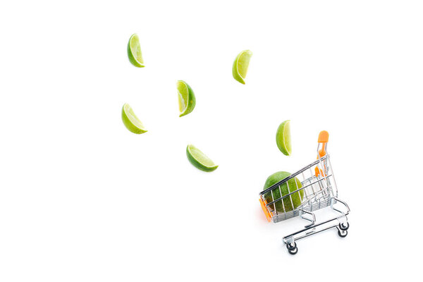top view of lime slices near decorative small shopping cart isolated on white