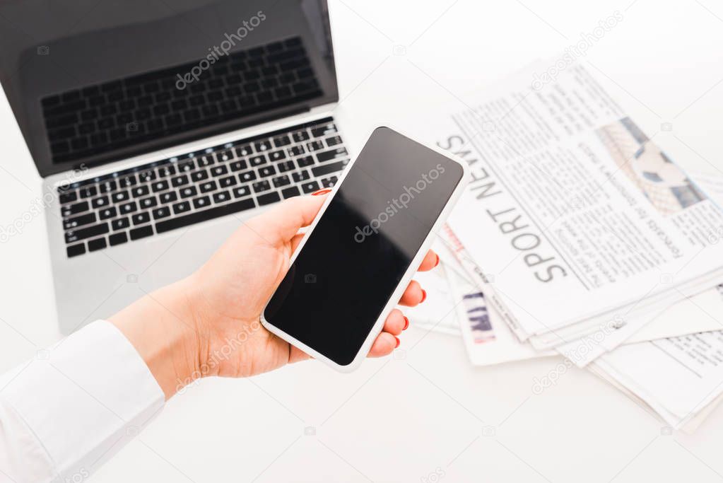 selective focus of woman holding smartphone with blank screen near laptop and  newspapers with sport news