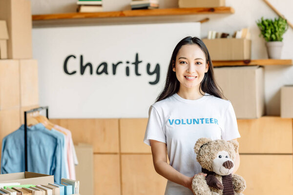 beautiful asian volunteer girl with teddy bear smiling and looking at camera