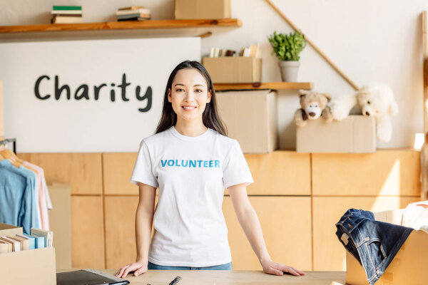 smiling asian girl in white t-shirt with volunteer inscription smiling and looking at camera