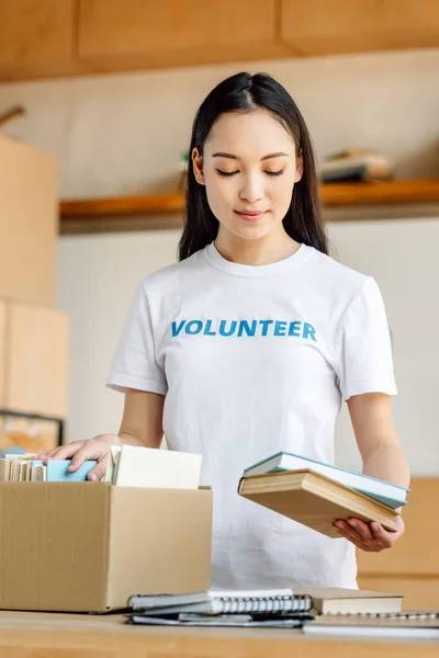 Pretty Concentrated Asian Volunteer Unpacking Cardboard Box Books — Stock Photo, Image