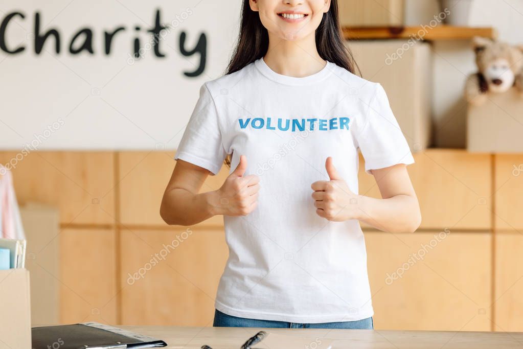 partial view of young woman in white t-shirt with volunteer inscription showing thumbs up 