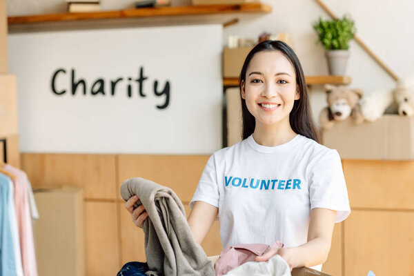 young asian volunteer girl unpacking cardboard box with clothes