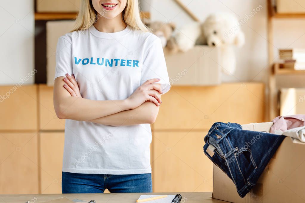 cropped view of volunteer standing with crossed arms near carton box with clothes