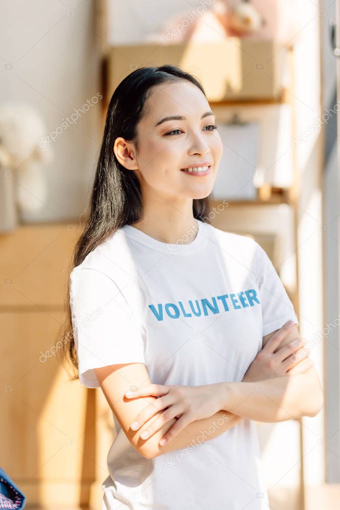 beautiful asian volunteer smiling while standing with crossed arms and looking away
