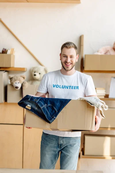 Gutaussehender Fröhlicher Freiwilliger Hält Karton Mit Kleidung Der Hand — Stockfoto