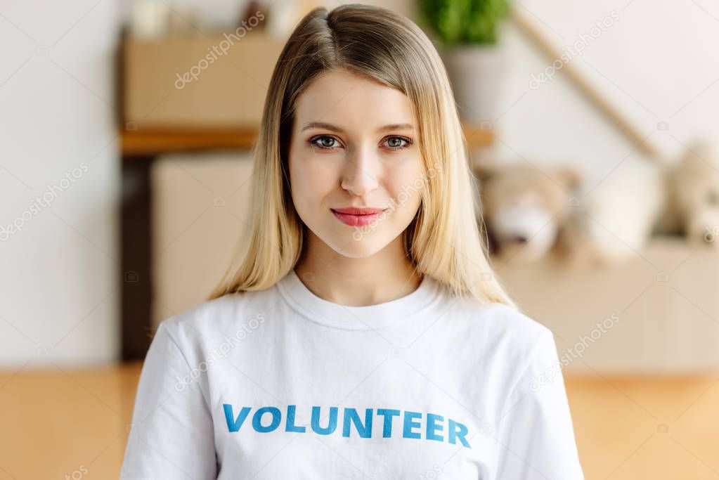 beautiful blonde girl in white t-shirt with volunteer inscription smiling and looking at camera