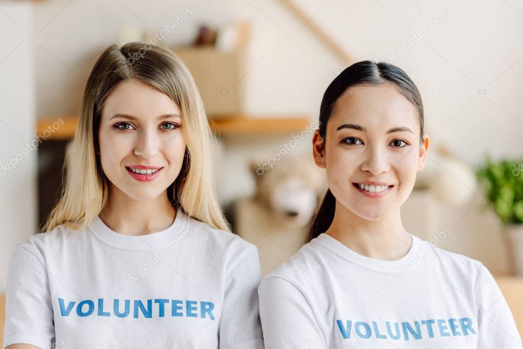 two beautiful multicultural volunteers in white t-shirts smiling and looking at camera