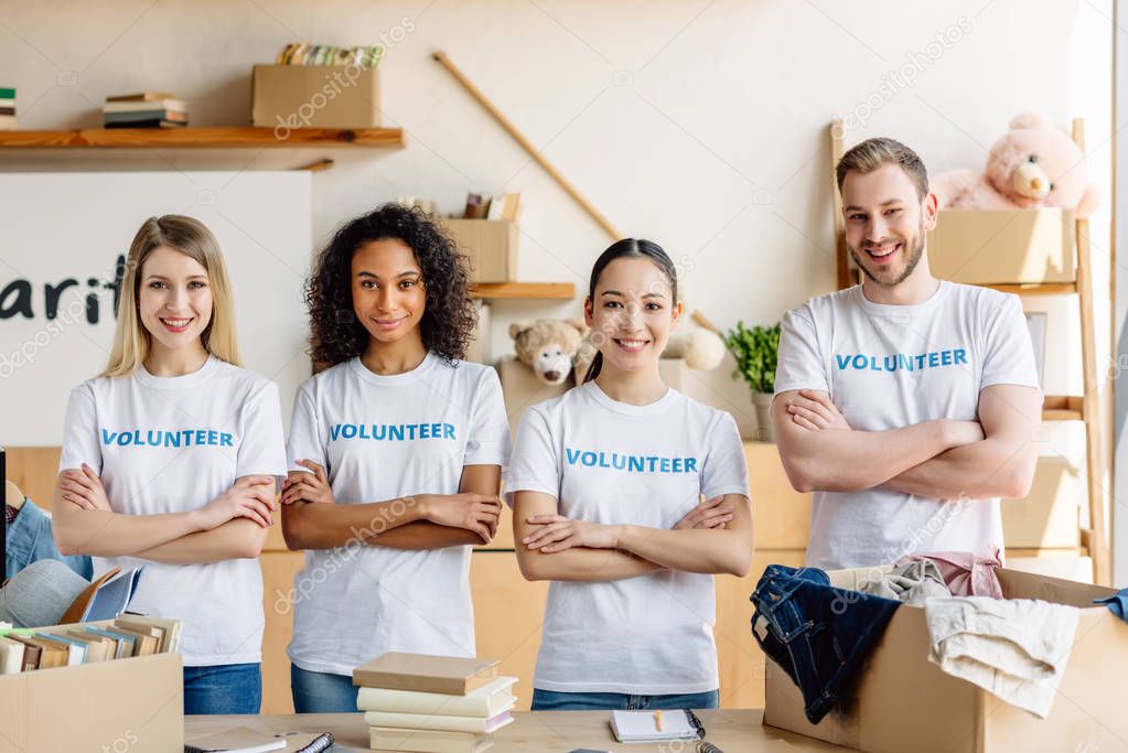 four smiling young volunteers in white t-shirts with volunteer inscriptions smiling and looking at camera