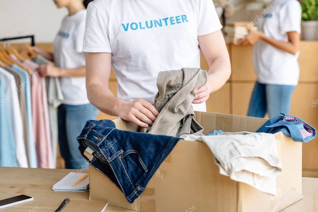 cropped view of volunteer unpacking cardboard box with clothes