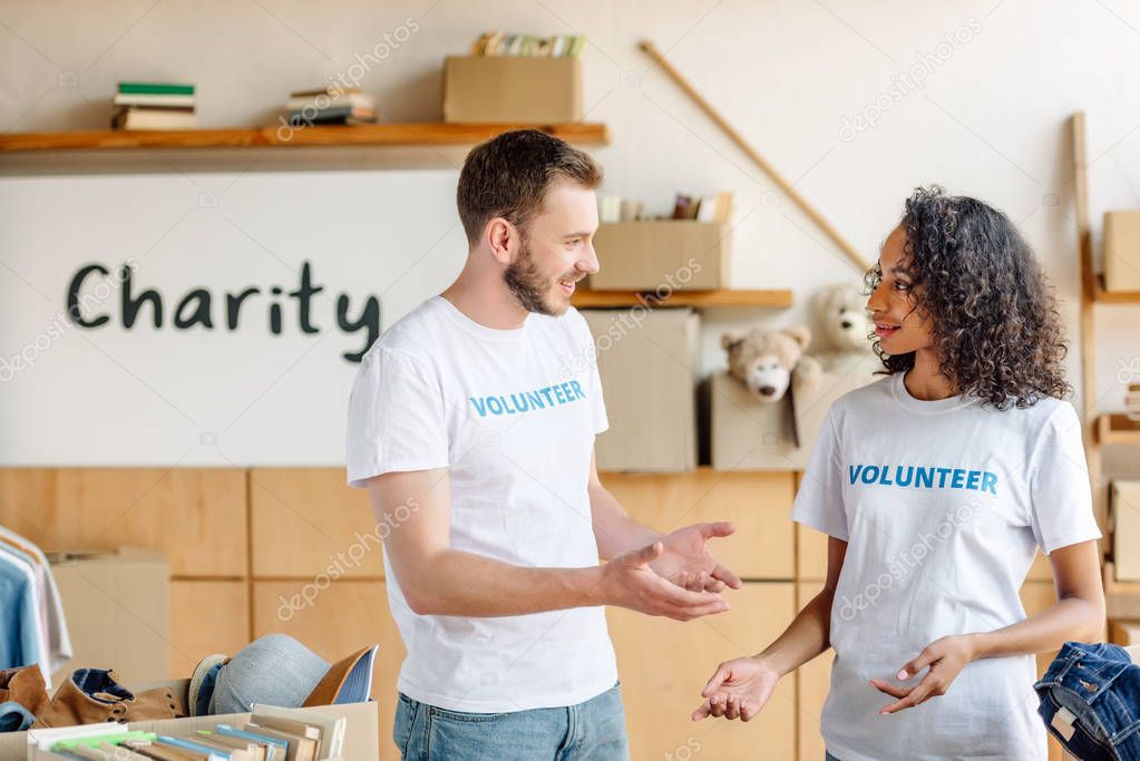 two multicultural volunteers talking while standing near carton boxes with books and clothes