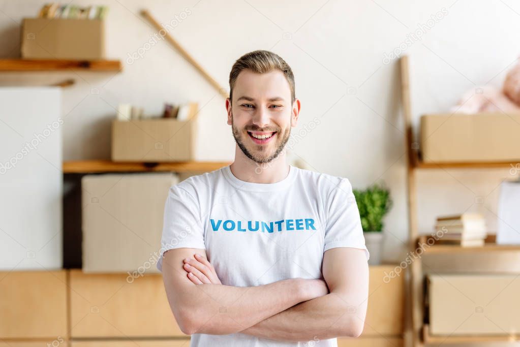 handsome young volunteer with crossed arms smiling and looking at camera