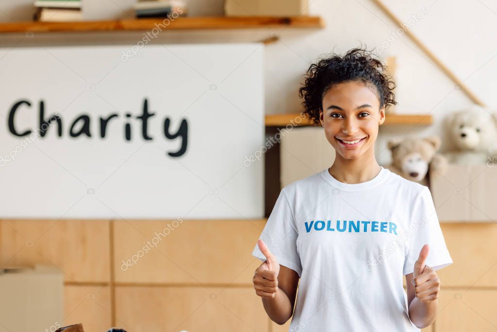 pretty african american volunteer girl showing thumbs up and looking at camera