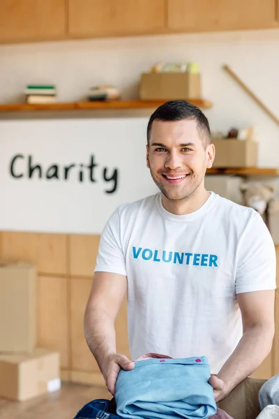 Guapo Voluntario Sonriente Sosteniendo Ropa Mirando Cámara Centro Caridad — Foto de Stock