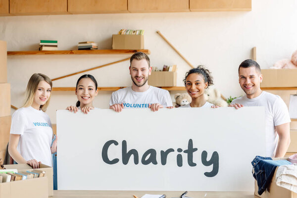 five young, multicultural volunteers holding placard with charity inscription