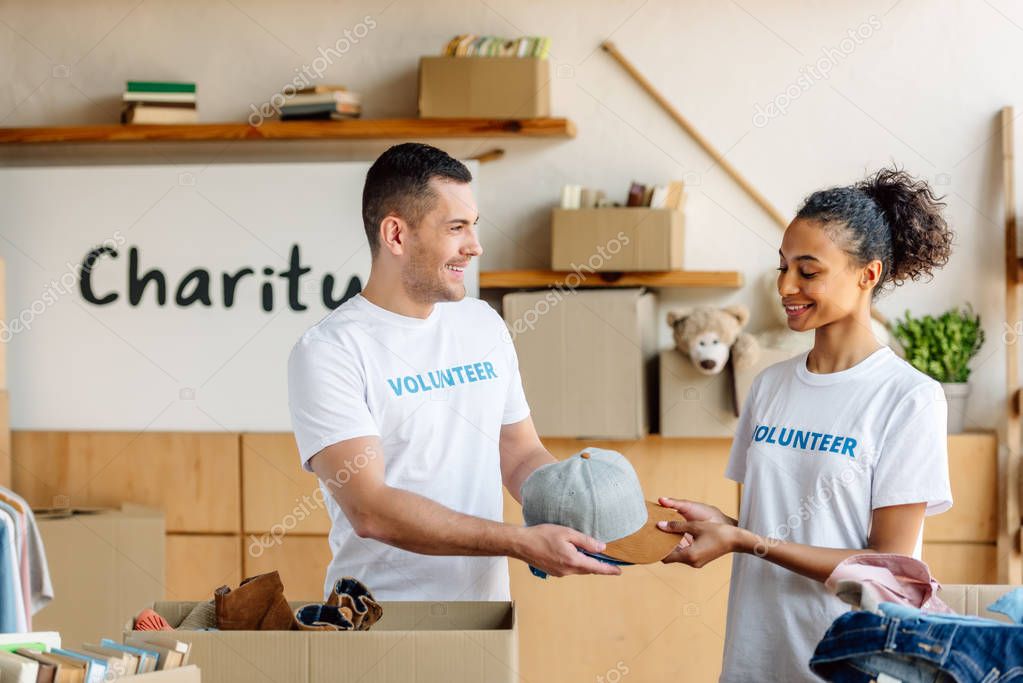 two smiling multicultural volunteers standing near carton boxes with clothes and books