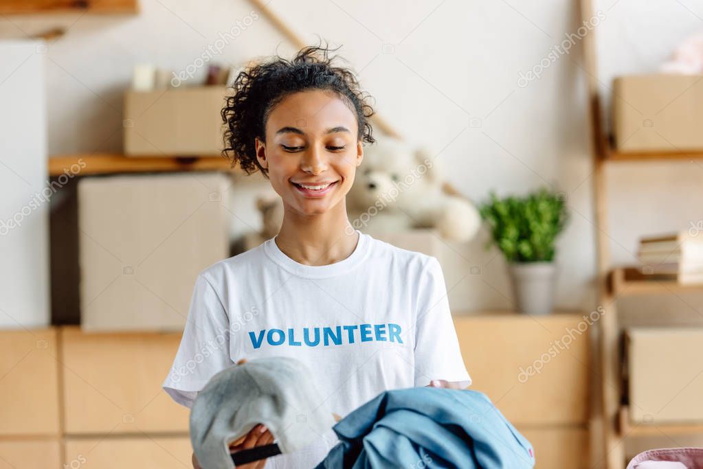 beautiful african american girl in white t-shirt with volunteer inscription holding clothes 