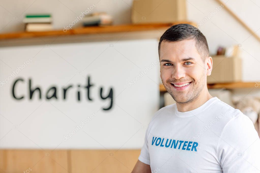 handsome, smiling volunteer standing near placard with charity inscription