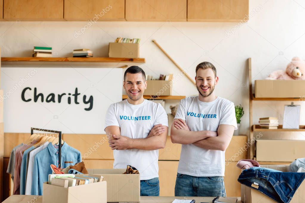 two cheerful, handsome volunteers standing with crossed arms and looking at camera