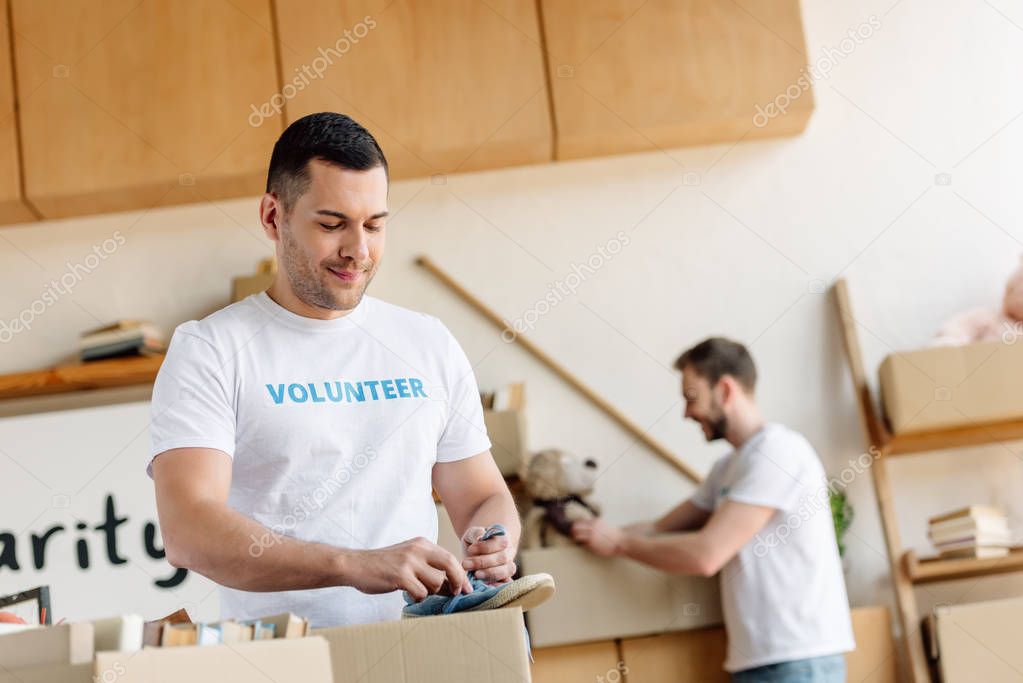 selective focus of handsome volunteer unpacking cardboard box with footwear