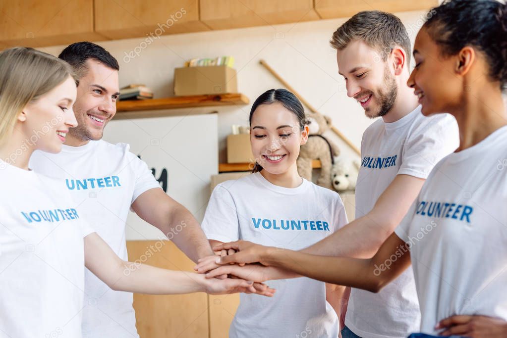 five young multicultural volunteers smiling and holding hands in charity center