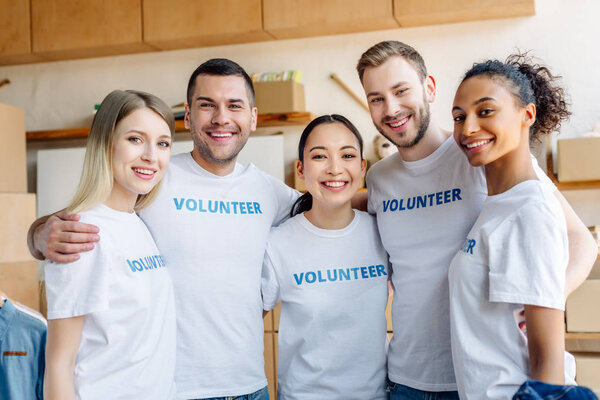 group of five young, multicultural volunteers embracing, smiling and looking at camera