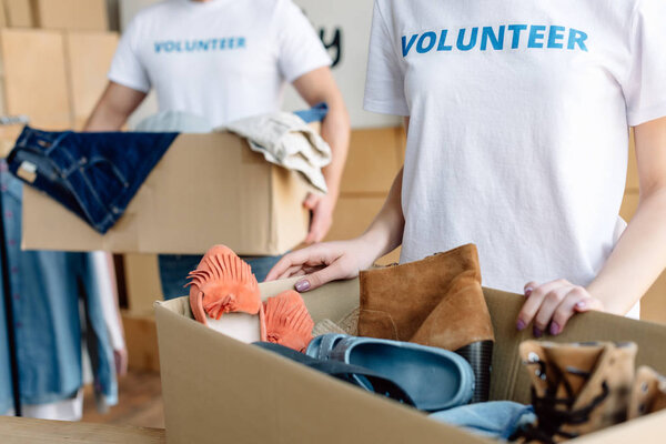 partial view of volunteers unpacking cardboard boxes with clothes and footwear