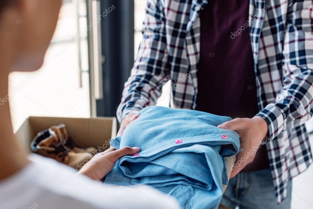 cropped view of man taking clothes from african american volunteer 