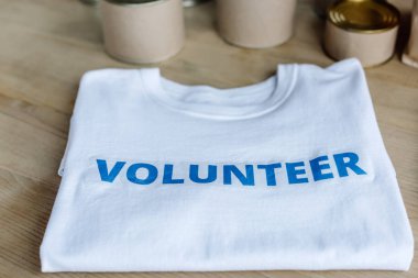 selective focus of white t-shirt with blue volunteer inscription on wooden table clipart