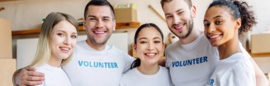 panoramic shot of young, cheerful volunteers hugging and looking at camera clipart