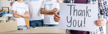 panoramic shot of man holding card with thank you inscription while standing near volunteers clipart