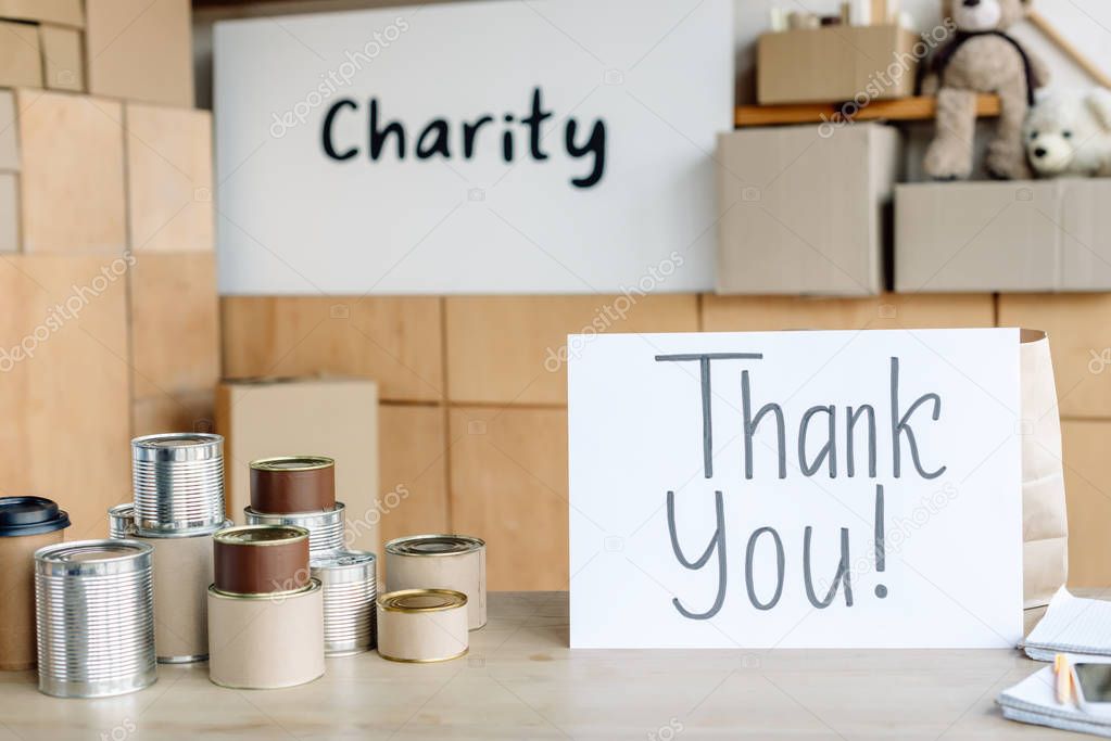 card with thank you inscription, canned food and disposable cups in charity center