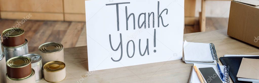 panoramic shot of wooden table with tins, notebooks and card with thank you inscription