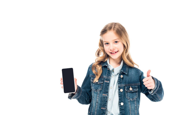 smiling kid in denim jacket holding smartphone with blank screen and showing thumb up isolated on white