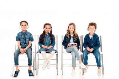 four kids in denim clothes sitting on chairs and listening music in headphones on white clipart