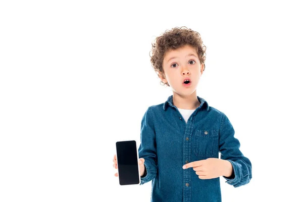 白で隔離された空白の画面でスマートフォンに指を向けるデニムシャツでショックを受けた子供の正面図 — ストック写真
