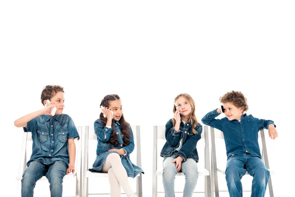 四个孩子穿着牛仔服坐在椅子上 在智能手机上交谈 隔离在白色 — 图库照片
