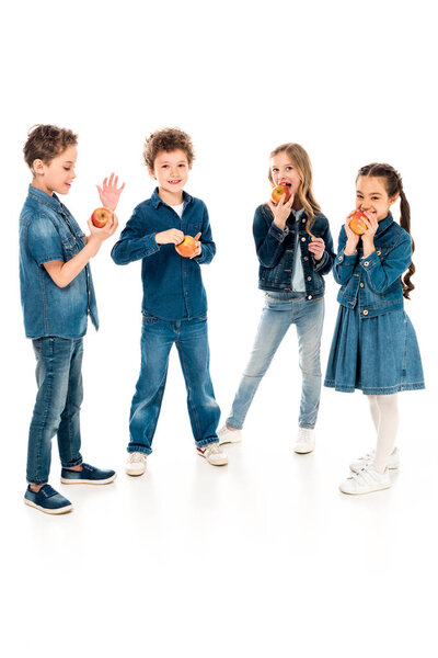 полный вид на детей в джинсовой одежде, поедающих яблоки на белом
