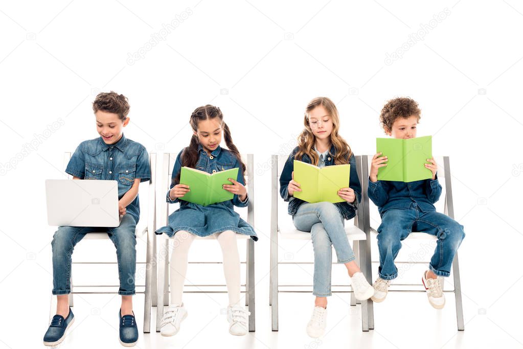 smiling boy using laptop while his friends reading books on white