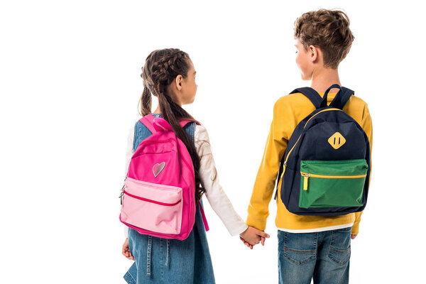 back view of schoolchildren with backpacks holding hands isolated on white