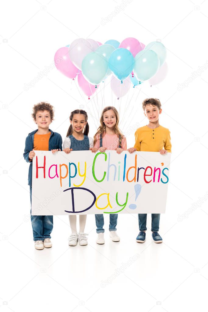 full length view of kids holding colorful balloons and placard on white