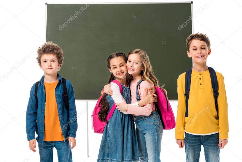 smiling schoolgirls embracing near blackboard isolated on white