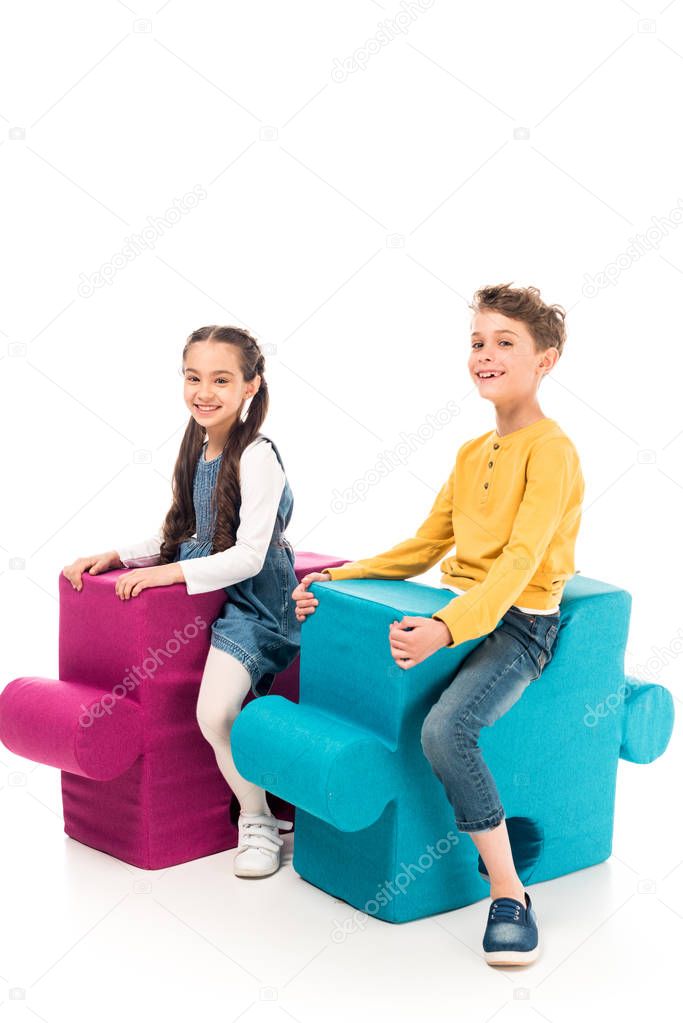 smiling kids sitting on big jigsaw puzzles isolated on white