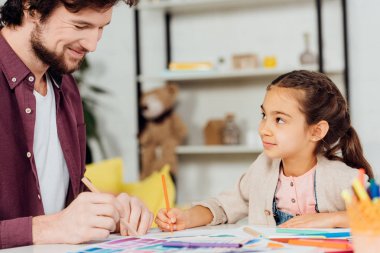 evde çizim mutlu ve yakışıklı baba bakarak sevimli kızı seçici odak 