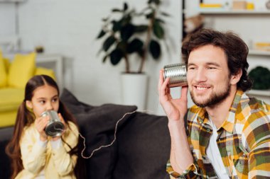 selective focus of cheerful father holding can phone while kid talking at home