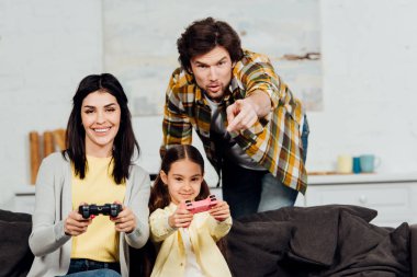 yakışıklı adam evde video oyunu oynarken yakın parmak ile işaret neşeli karısı ve çocuk 